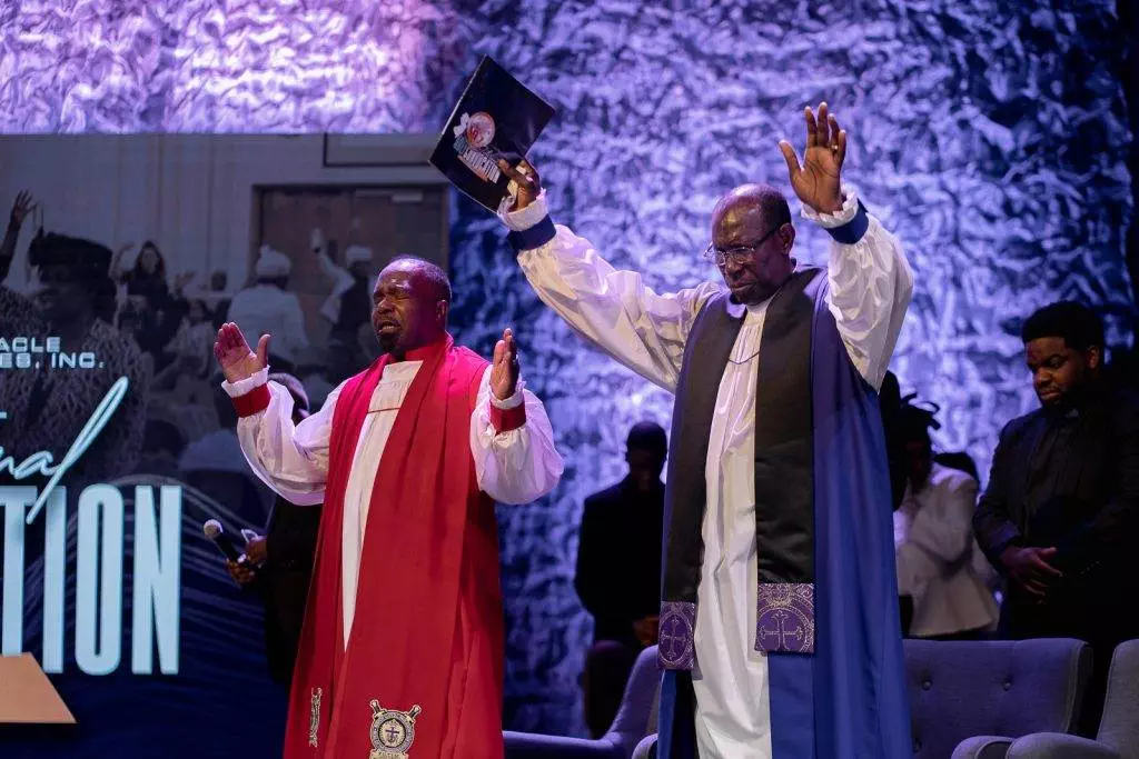 Two apostolic men in robes standing in front of a stage.