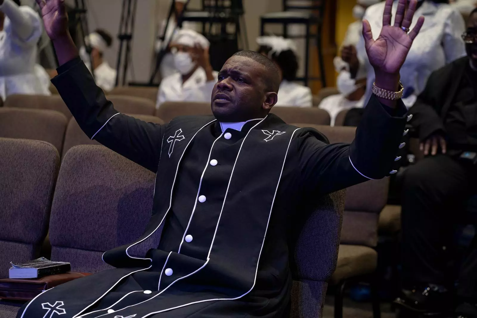 An apostolic man is sitting in a church with his hands raised.